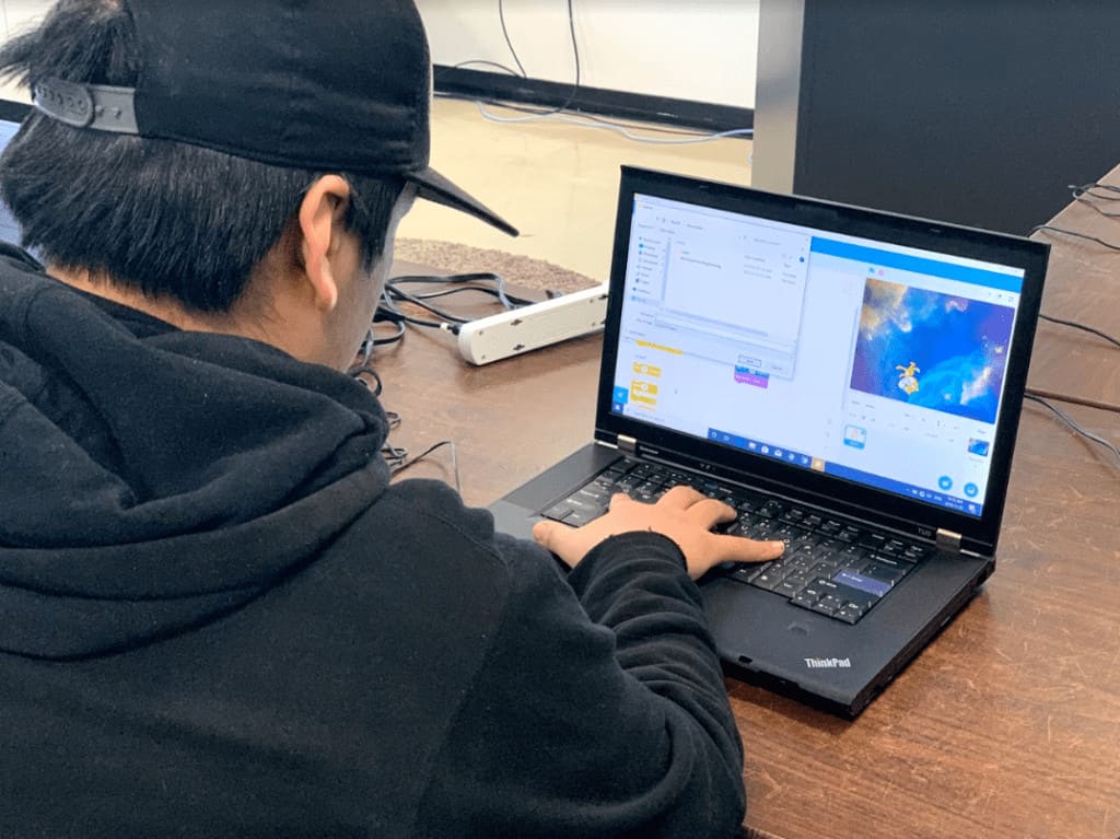 Young man wearing black hoodie and black cap working on a laptop, Digital Skills camp Kuujjuaq