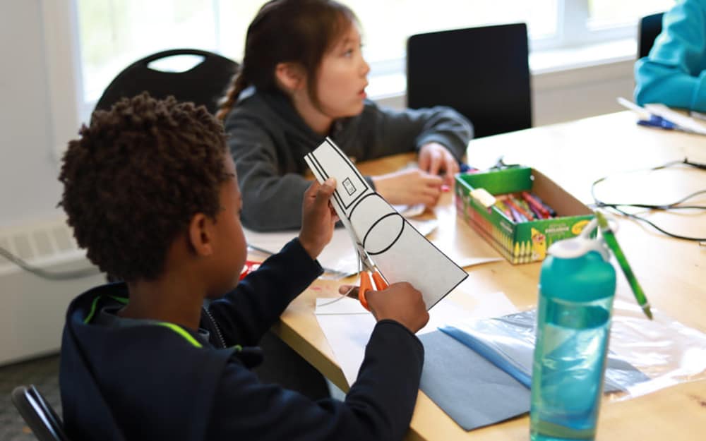 A student using scissors to cut out a paper flashlight.