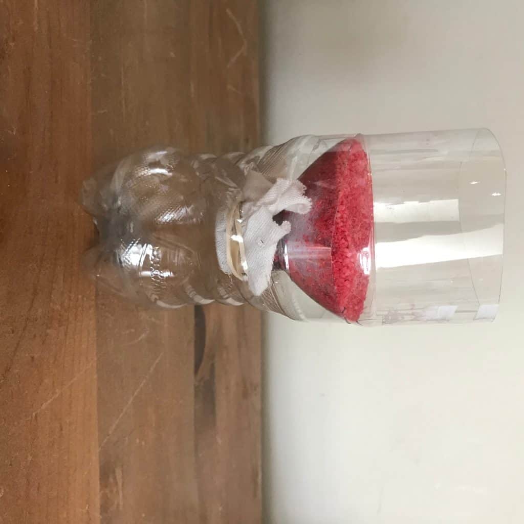 The water bottle with red sand inside of it.
