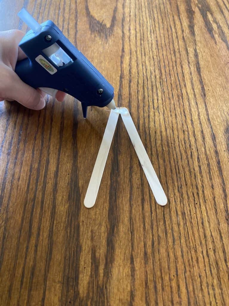 Hot gluing two popsicle sticks together laying in a triangle shape.