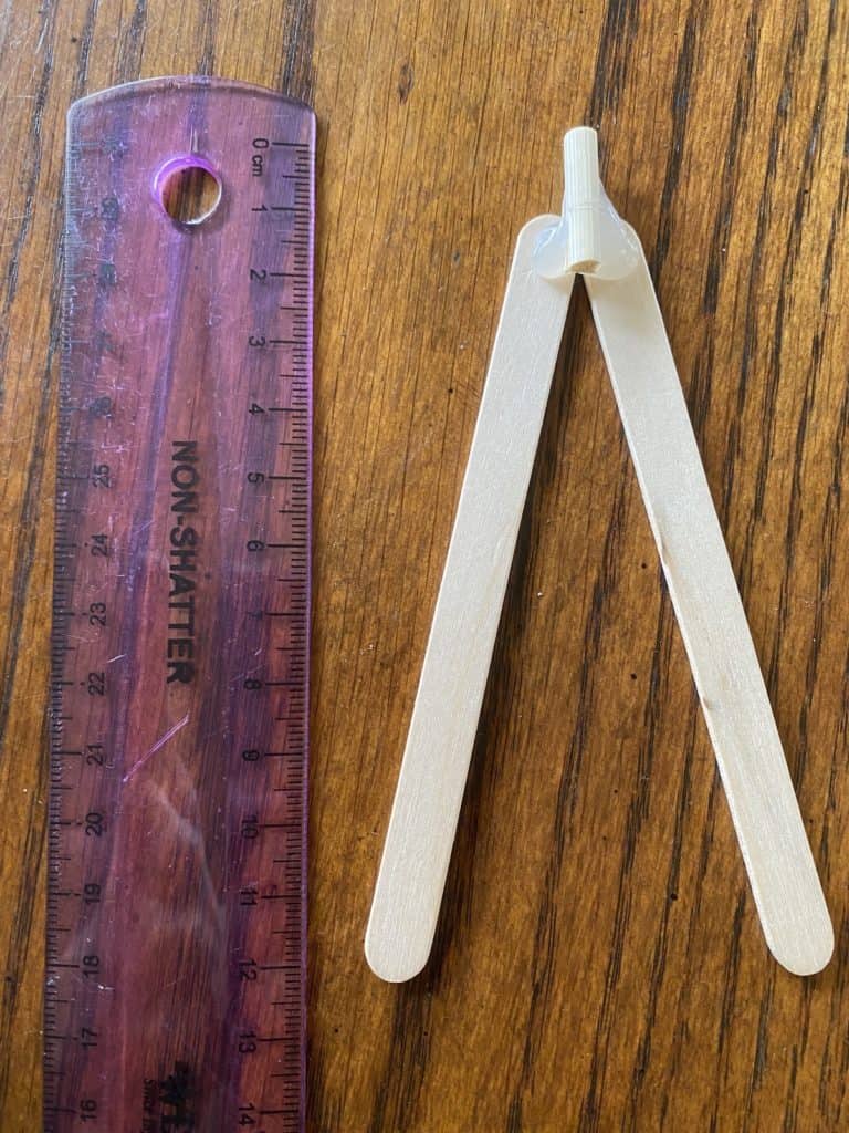A ruler beside two popsicle sticks laying together on a wooden table.