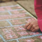 A kid drawing with chalk on pavement.