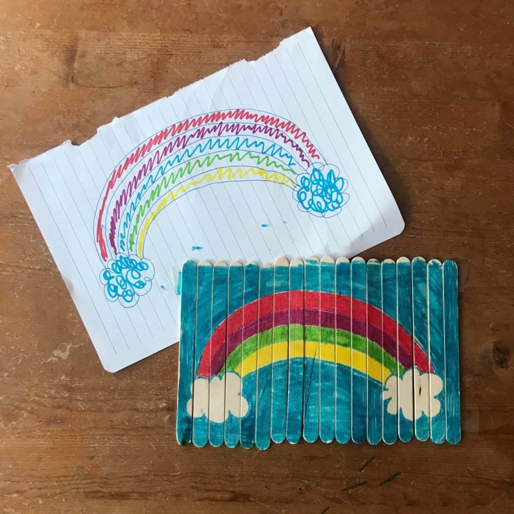 A rainbow puzzle made with popsicle sticks laying on top of a drawn picture of a rainbow.