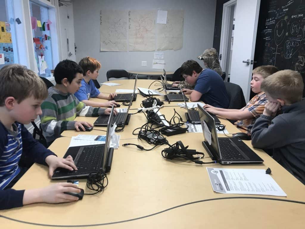 Students working on laptops on the left and right side of a beige table.