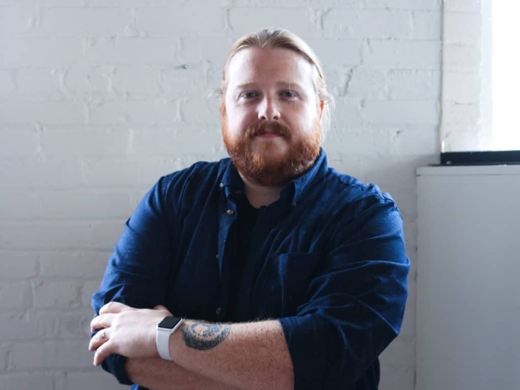 Aaron Labbe, founder of Lucid standing in front of a white wall with his arms crossed across his chest.