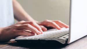 Person sitting at a table with their hands resting on a laptop keyboard.