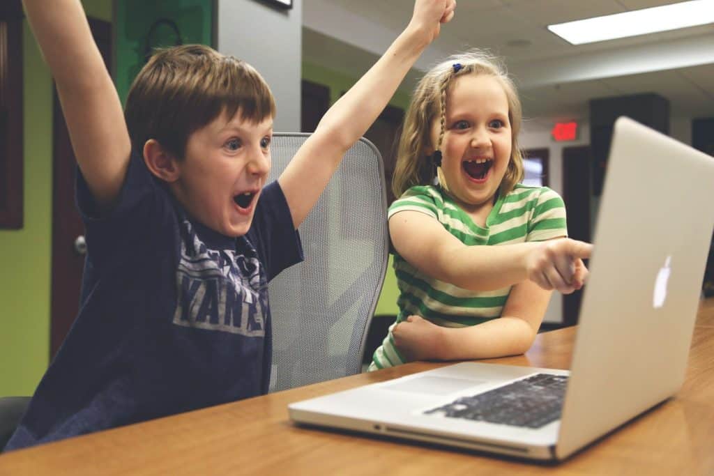 kids playing games with a computer in front of them. They both look excited.