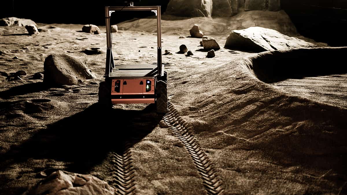 The Mission Control Space Services Rover in motion on Mars, with a rocky background