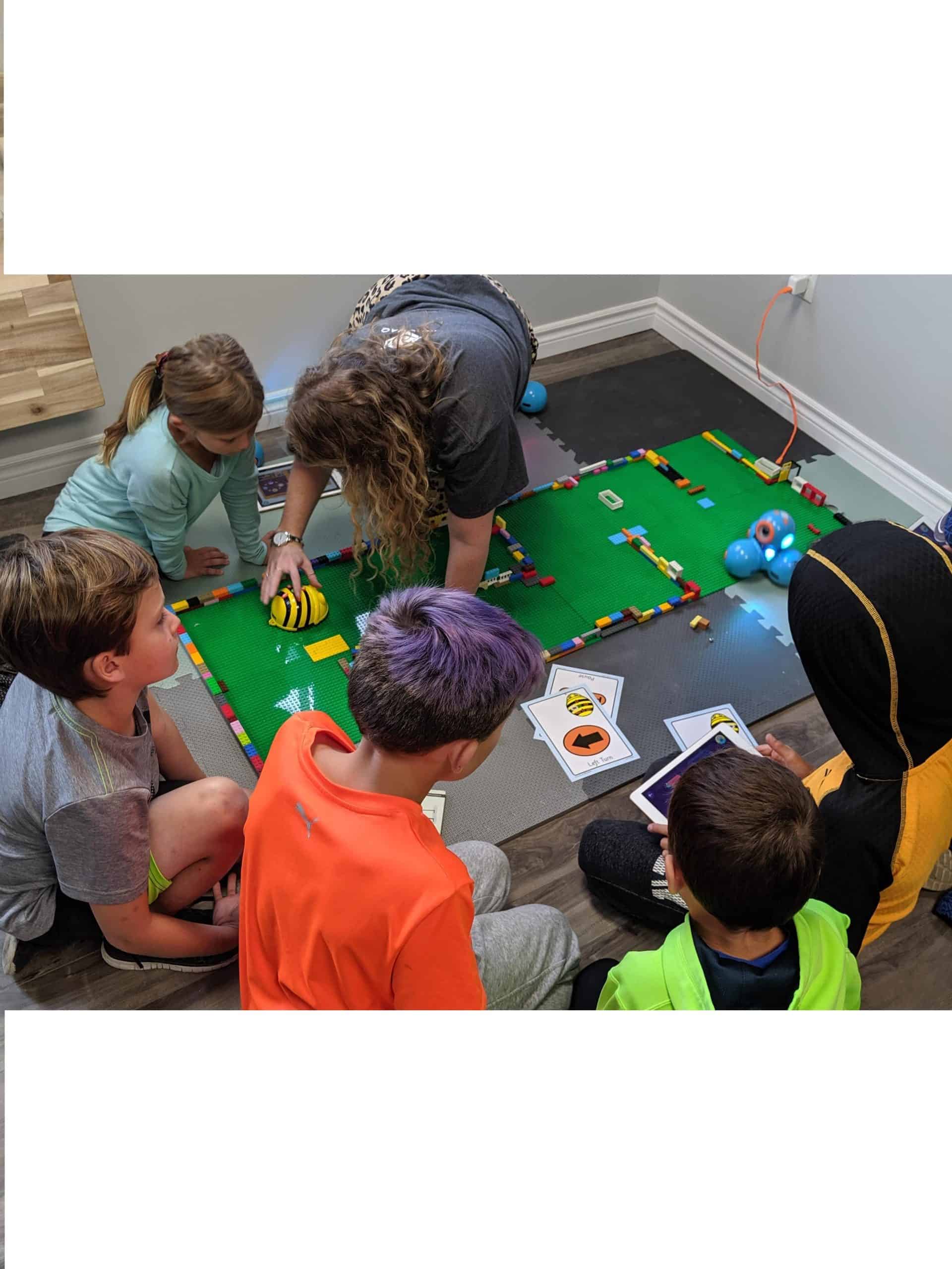 5 kids kneeling around a mat and building a lego obstacle courses for robots with an instructor kneeling beside