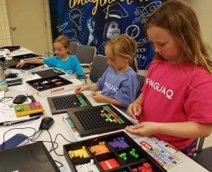 three girls in pinnguaq camp shirts building game levels using plastic blocks