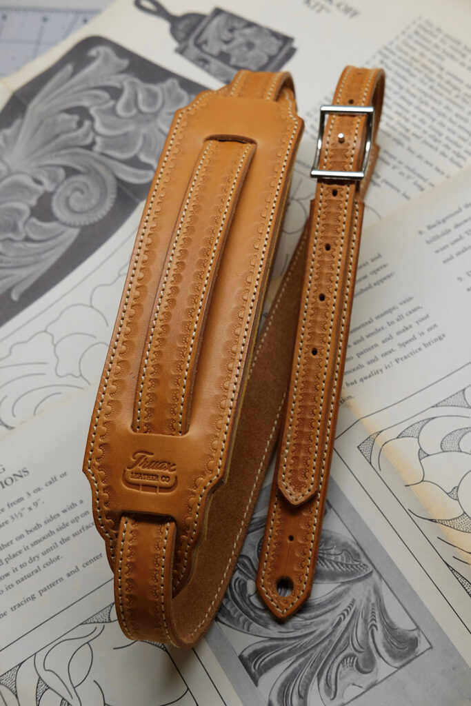 A tan leather guitar strap lays atop a spread of printed designs.