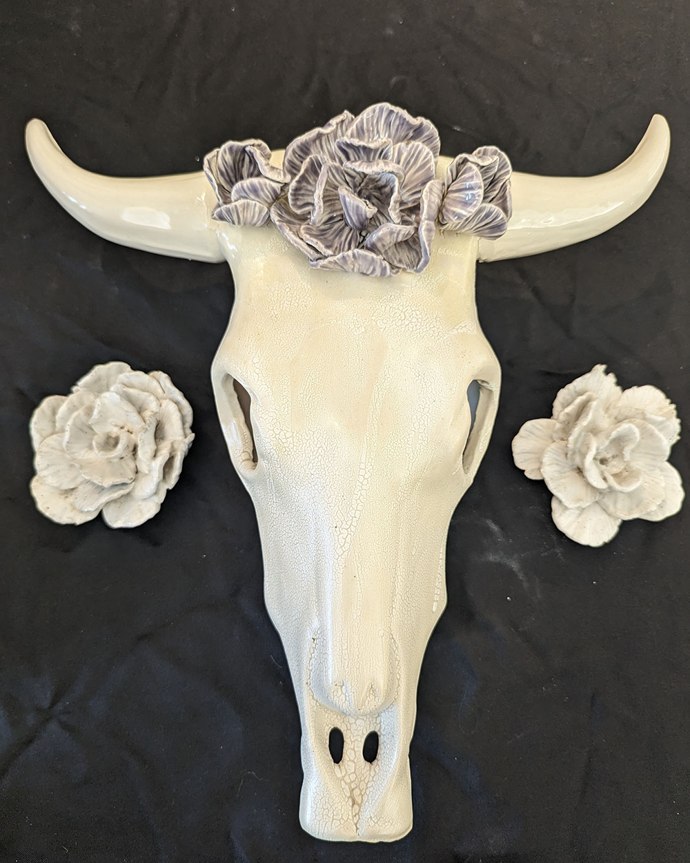 A ceramic mold of an animal's horned skull sits between two white ceramic flowers.