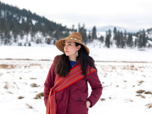 A person stands in front of a snowy, wooded landscape, looking to their right.